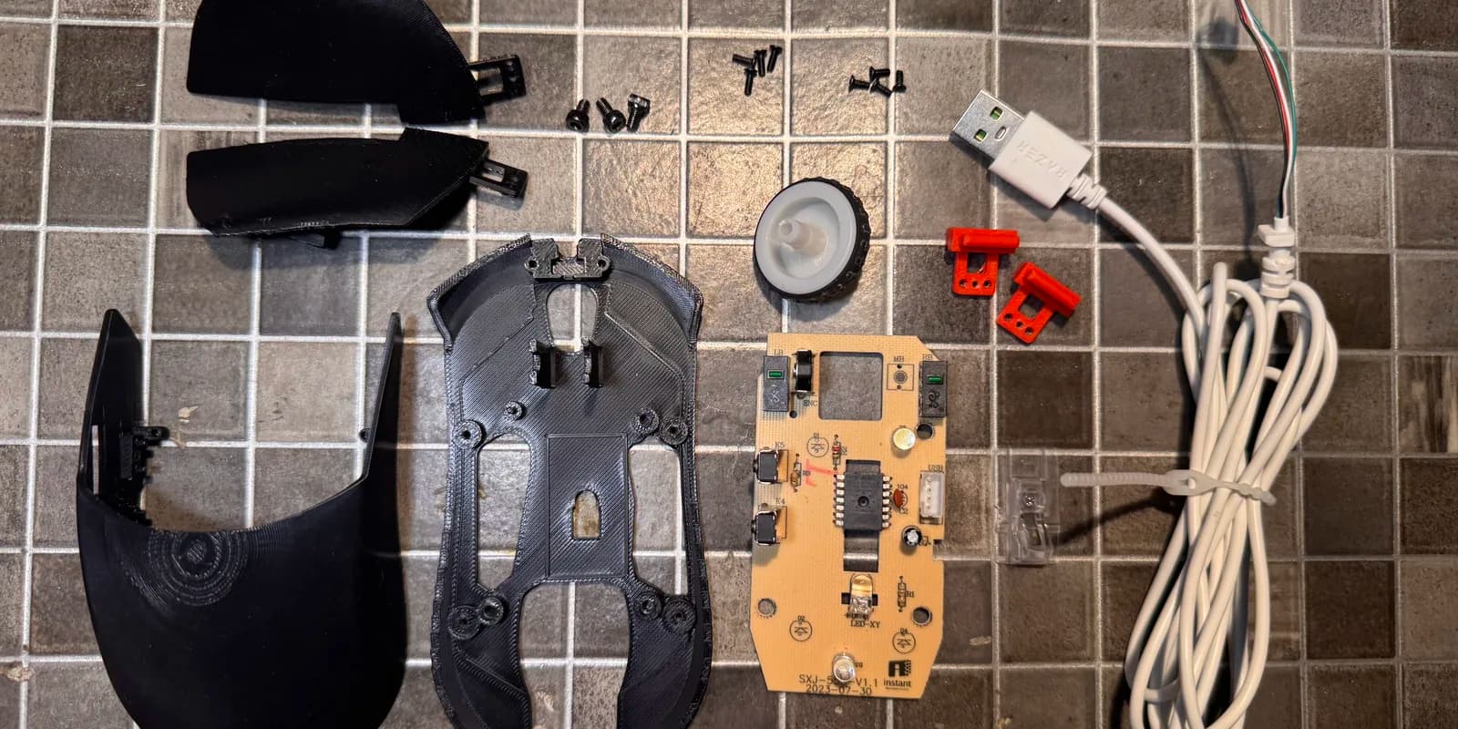 The printed mouse shell, base plate, buttons, PCB and screws laid out on a table